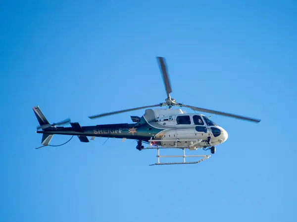 Sheriff's helicopter with a camera turret and searchlight, in flight against a blue sky