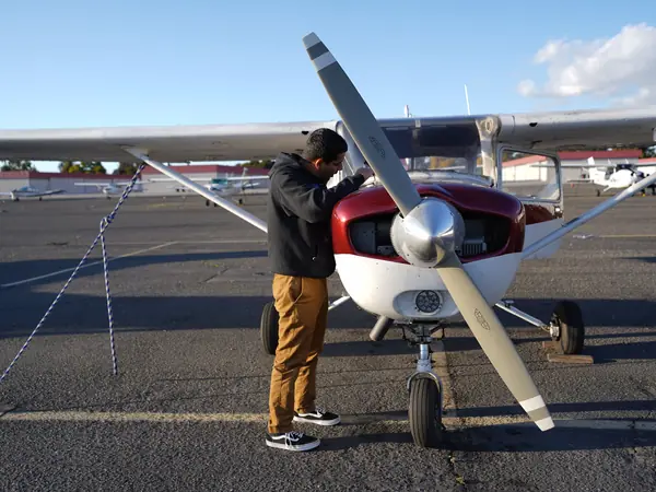 Owner-pilot checking the engine cowling of a red and white Cessna on the ramp